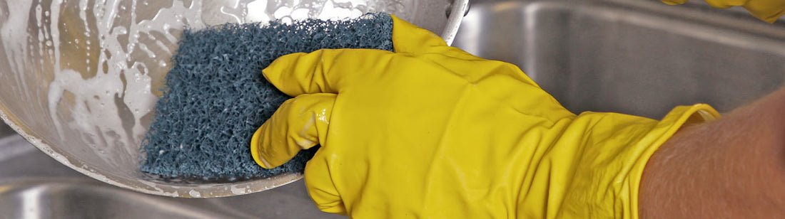 Person wearing yellow neptune gloves and cleaning a bowl with a sponge