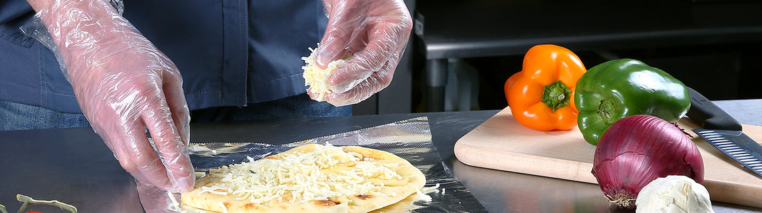 Person wearing clear poly gloves and adding toppings to a pizza