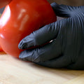 Person wearing black nitrile gloves and slicing a tomato