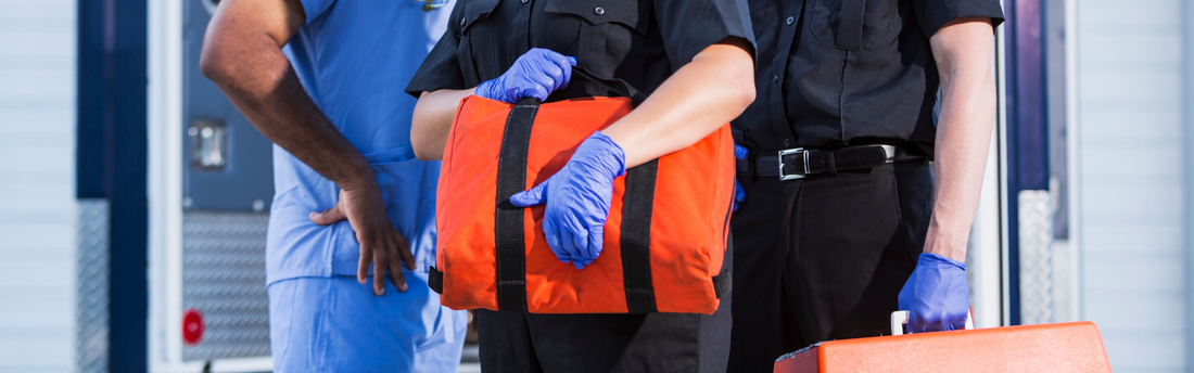 Two first responders in nitrile gloves next to a nurse in front of an ambulance