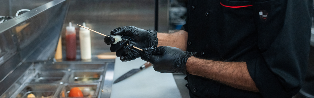 chef wearing black vitrile gloves and preparing skewers