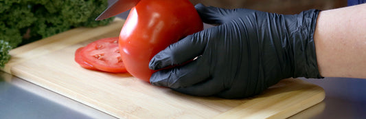Person wearing black nitrile gloves and slicing a tomato