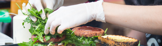 person wearing white disposable gloves and prepping a burger