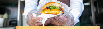 person wearing poly gloves and holding a fresh burger